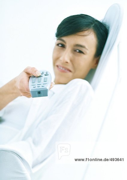 Woman sitting back  smiling  and pointing remote control at camera