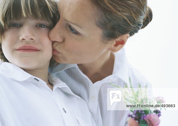 Mother with small bouquet of flowers kissing son on cheek