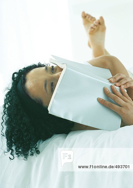 Frau im Bett liegend  Gesicht mit Buch bedeckend