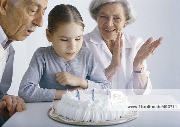 Mädchen mit Großeltern  versammelt um Geburtstagskuchen