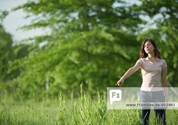 Woman standing outdoors pointing toward ground