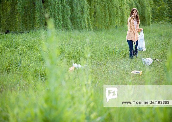 Frau sammelt Abfall im Feld auf  zeigt auf die Kamera