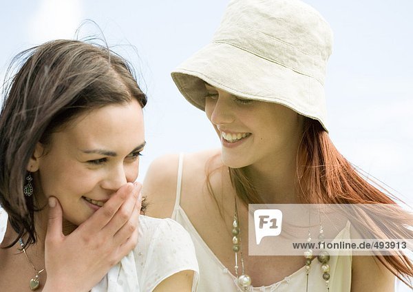 Zwei junge Frauen lächeln  eine deckt den Mund.