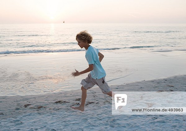Junge rennt am Strand bei Sonnenuntergang