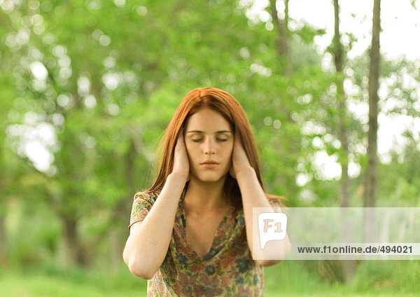 Woman with hands over ears and eyes shut  outdoors