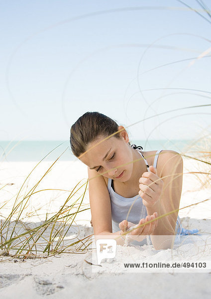Girl lying on beach  letting sand run through hands