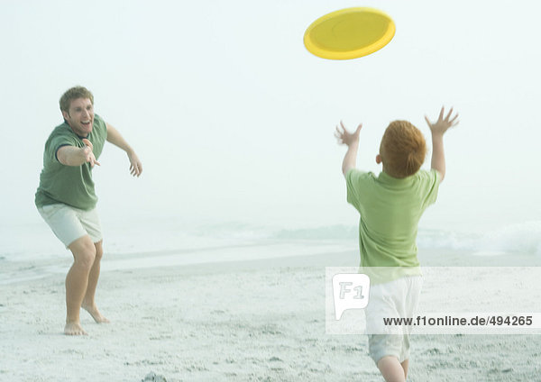 Vater und Sohn werfen Frisbee an den Strand