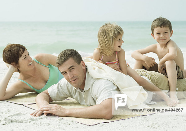 Familie am Strand  Eltern liegen auf der Matte  Kinder sitzen auf dem Rücken des Vaters.