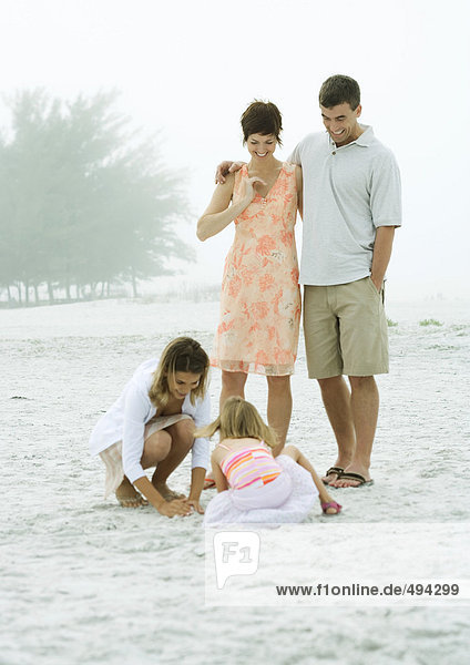 Familie am Strand  Eltern beobachten Töchter beim Spielen im Sand