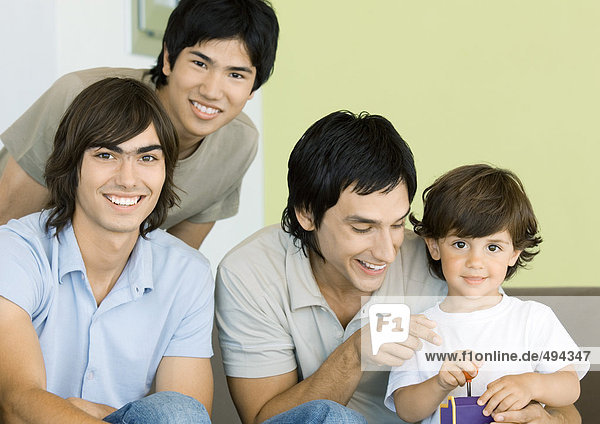 Three young men and little boy playing video games