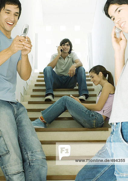 Vier junge Leute benutzen Handys im Treppenhaus