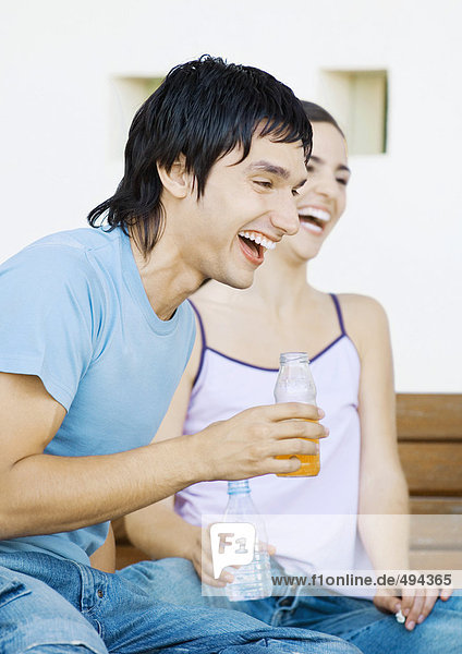 Two young adult friends with bottles laughing