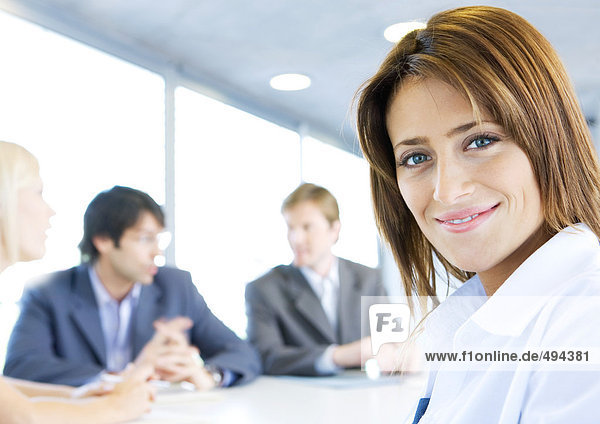 Businesswoman smiling at camera  meeting in background