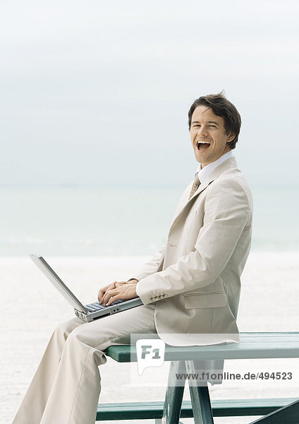 Geschäftsmann sitzt am Rand des Picknicktisches am Strand  mit Laptop