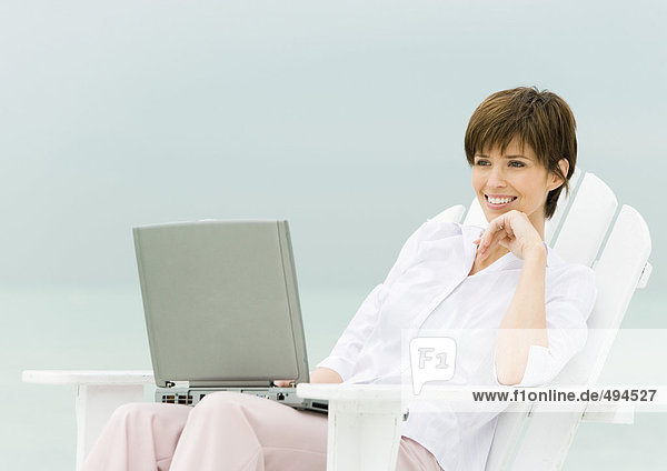 Frau sitzt im Liegestuhl mit Laptop  Meer im Hintergrund