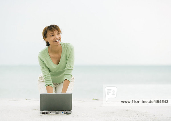 Frau am Strand  kniend auf Sand mit Laptop