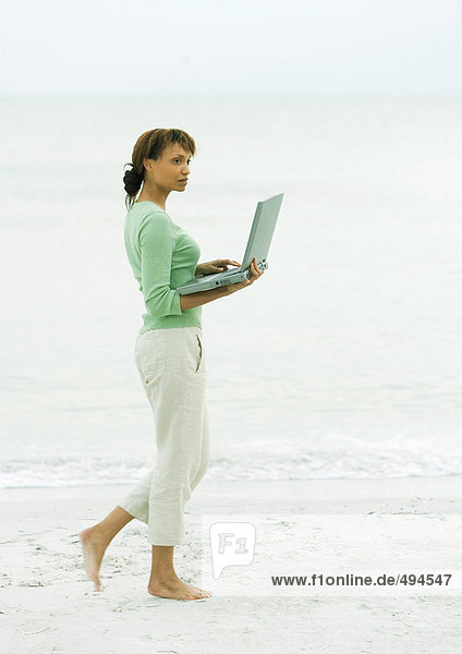 Frau  die am Strand spazieren geht  mit offenem Laptop
