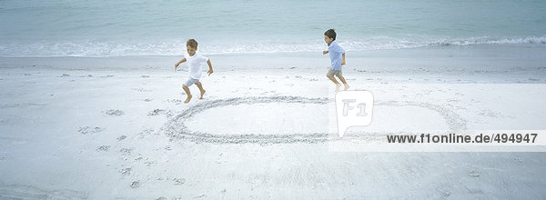 Zwei Jungen  die am Strand in Form rennen