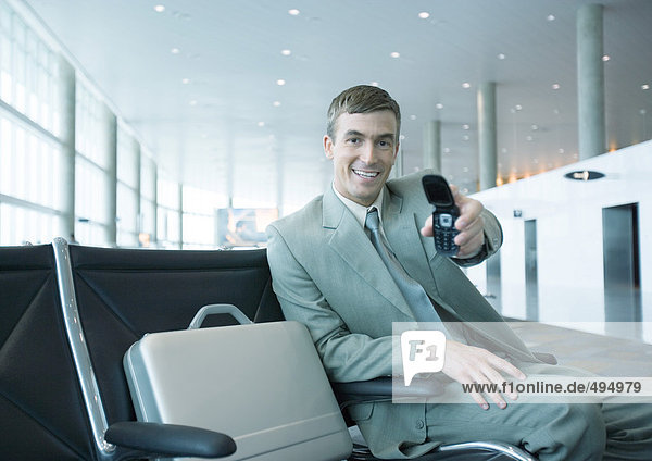 Businessman holding out cell phone in airport lounge