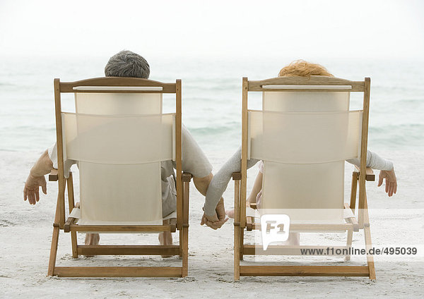 Paar in Strandkörben sitzend  Händchen haltend  Rückansicht