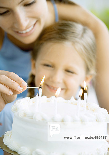Mutter entzündet Kerzen auf Geburtstagskuchen für Tochter