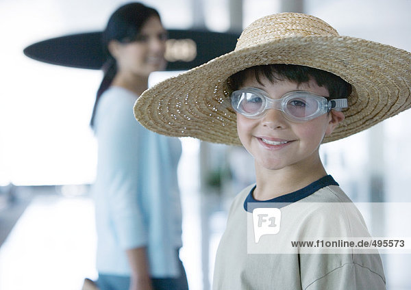 Junge mit Brille und Strohhut im Flughafen  lächelnd vor der Kamera
