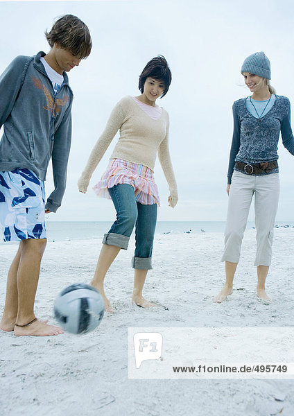 Drei junge erwachsene Freunde spielen Fußball am Strand