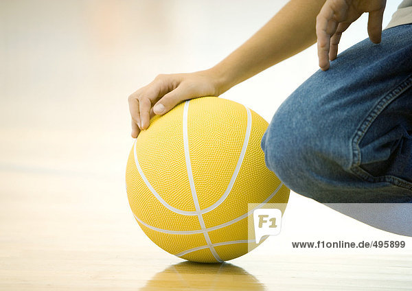 Jugendlicher Junge kauernd  Basketball haltend  Nahaufnahme von Hand auf Ball und Knie