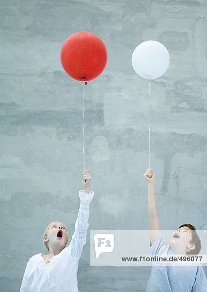 Zwei Kinder halten Luftballons und machen Gesichter