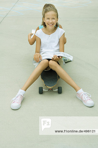 Zwei Mädchen sitzen Rücken an Rücken auf dem Skateboard und lesen