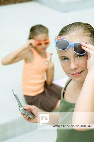 Girl lifting sunglasses and holding cell phone