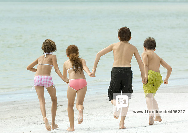 Vier Kinder halten sich an den Händen und rennen zum Wasser  am Strand  Rückansicht