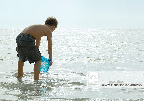 Boy filling bucket with water in surf