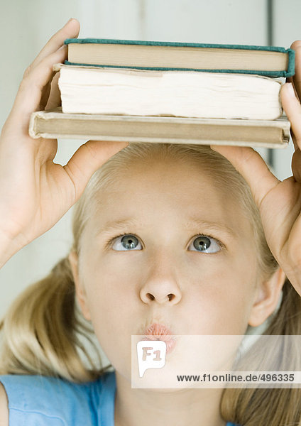 Mädchen hält Bücherstapel auf dem Kopf  kreuzende Augen