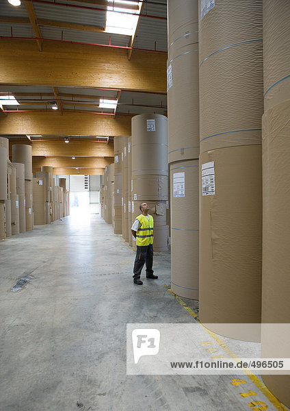 Factory worker standing next to rolls of paper