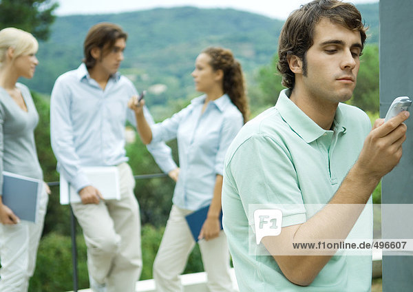 Lässig gekleidete junge Führungskräfte bei der Arbeit im Freien  Mann im Vordergrund beim Überprüfen von Handy-Nachrichten