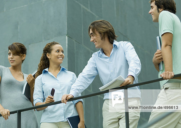 Vier junge Führungskräfte stehen neben dem Geländer  ein Mann und eine Frau lächeln sich an.
