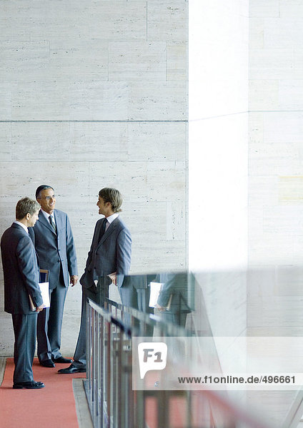 Three businessman standing  talking at end of corridor