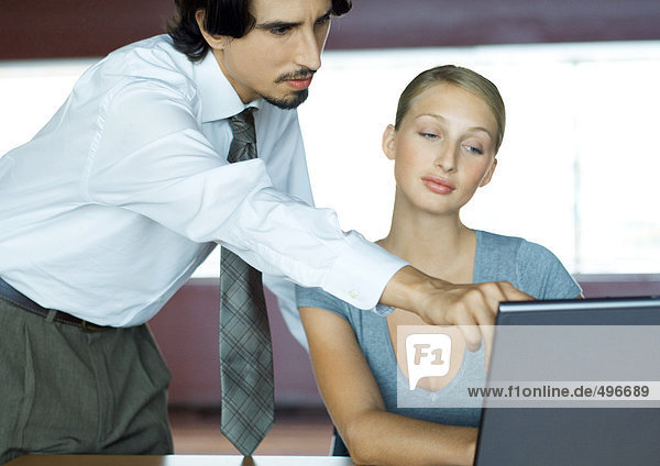 Businessman helping businesswoman with laptop