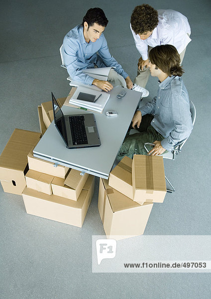Drei männliche Kollegen gruppiert um das Handy auf dem Schreibtisch  umgeben von Pappkartons