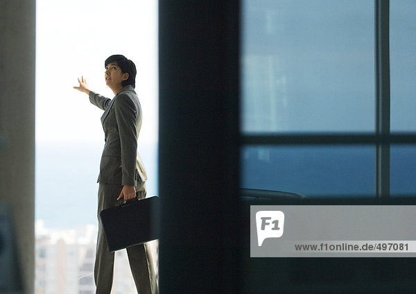Woman standing with briefcase  next to bay window with arm out  looking over shoulder