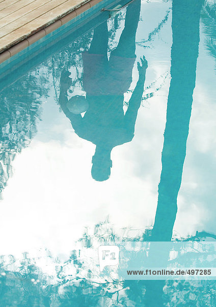 Mann steht am Rand des Schwimmbeckens  reflektiert in der Wasseroberfläche