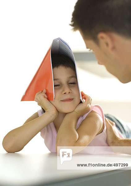 Mädchen hält Notizbuch über dem Kopf  dreht sich zum Vater.