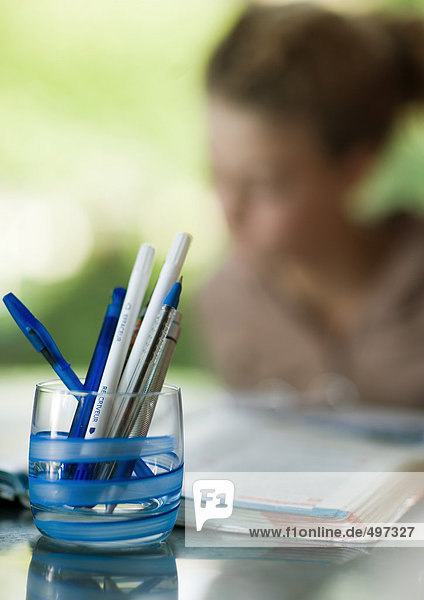 Glass full of pens  child doing homework in background