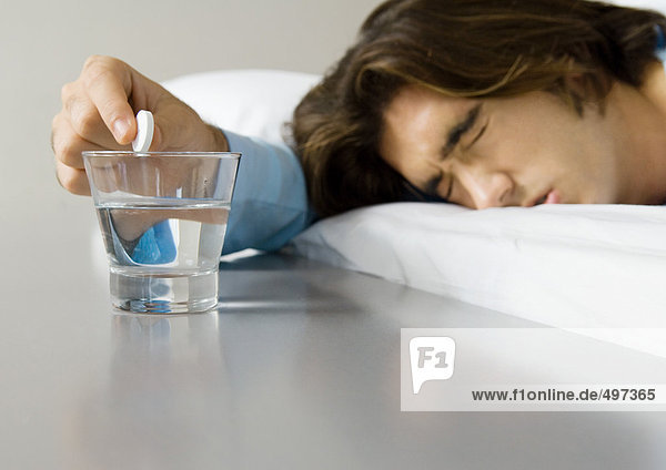 Mann im Bett liegend  schielende Augen zu und halten Brausemedizin über Glas Wasser.