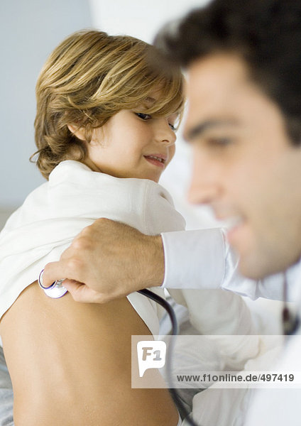 Arzt hält Stethoskop an den Rücken des Jungen