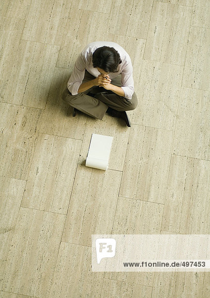 Man sitting on floor with blank pad of paper  high angle view
