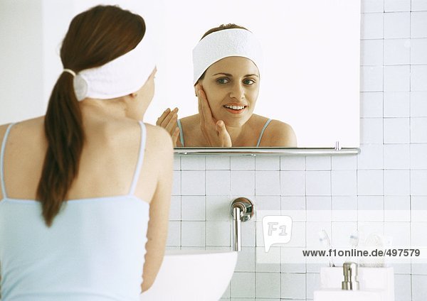 Woman looking in bathroom mirror  rubbing face