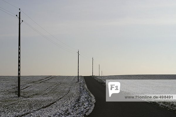 Landstraße in Landschaft mit Schnee auf Feldern