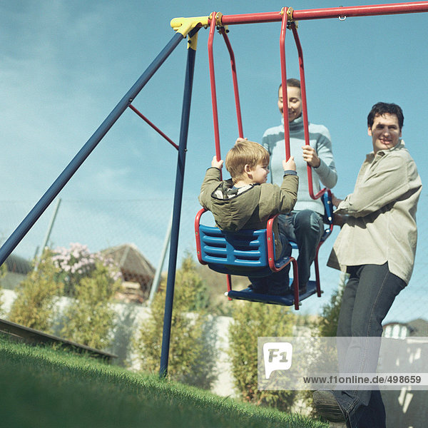 Man pushing wife and son on swing